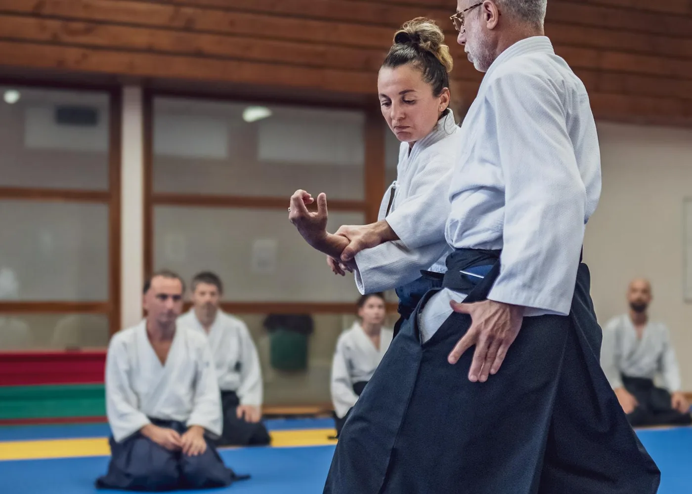 Deux pratiquants d'aïkido en keikogi et hakama travaillent une technique sur le tatami, corps ancré et posture stable