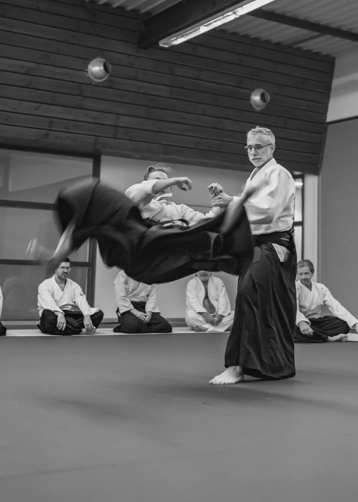 Deux pratiquants d'aïkido du dojo de Dardilly en plein mouvement, l'un accompagnant et redirigeant l'élan de l'autre, photo en noir et blanc